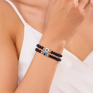 Detail van blauwe Evil Eye kralenarmbandenset in zwart en goud om een pols