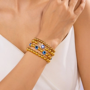 Detail van vier gouden kralenarmbanden met blauwe boze oog- en Hamsa-handhangers op de pols
