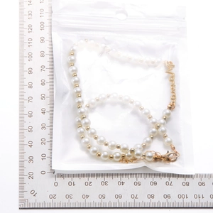 Détail du collier de perles MAMA avec lettrage doré à côté d'une règle pour la taille