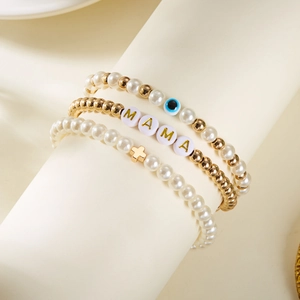 Makro-Detail des dreiteiligen MAMA Goldperlen- und Perlen-Armbandsets auf dem Ständer
