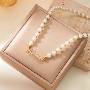Détail du pendentif doré Mama sur collier de perles blanches présenté dans un coffret à bijoux