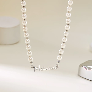 Gros plan du pendentif Mama sur un collier de perles blanches avec des billes argentées polies
