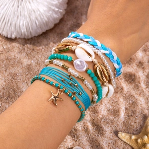 Detail of bohemian beach bracelet set with starfish charm and sea shells on sand