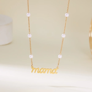 Gros plan détaillé du collier doré MAMA avec perles blanches sur une chaîne fine