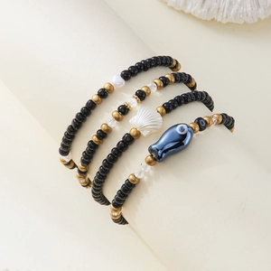 Primer plano de set bohemio de cuatro pulseras de cuentas con dijes de concha y pez