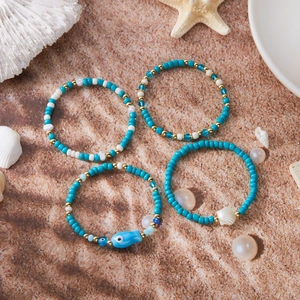 Set de 4 pulseras bohemias con conchas y peces sobre fondo de arena fina