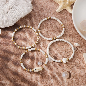 Detalle de cuatro pulseras bohemias con cuentas y dijes de pez y concha en fondo de arena