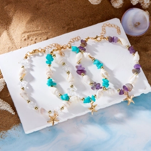 Detailsicht von Bohème-Seestern-Armbändern mit Muscheln und Türkissteinen auf Sand