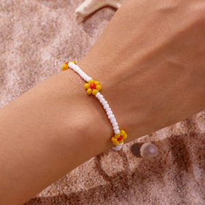 Detailopname van handgemaakte enkelband met witte kralen en gele bloemen op het strand