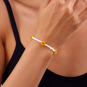 Detail van een handgemaakte enkelband met witte kralen en geel-oranje bloemmotieven