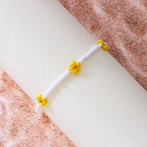 Detailopname van handgemaakte enkelband met witte kralen en gele madeliefjes