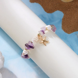 Detail eines Strandarmbands mit lila Kiessteinen, weißen Muscheln und goldenem Seestern