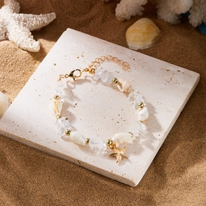 Nahaufnahme des böhmischen Seestern-Armbands mit Muscheln und Steinen auf Strandsand