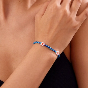 Detail van een handgemaakte boho enkelband met blauwe kralen en witte bloemaccenten