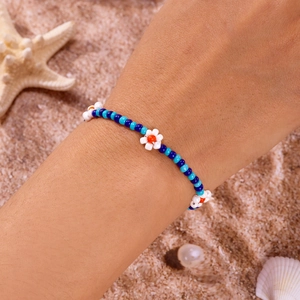 Detail van handgemaakte blauwe kralenarmband met witte bloemen op het strandzand