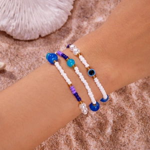 Boho-Armband-Set mit bösem Blick, Muscheln und Seesternen auf sandigem Strand