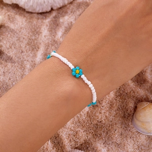 Detailopname van handgemaakte boho enkelband met witte kralen en blauw-gele bloemaccenten