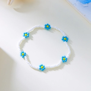 Detailweergave van handgemaakte witte kralen enkelband met blauwe bloemaccenten