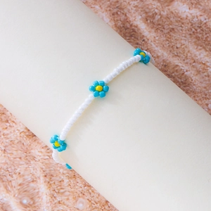 Detail van handgemaakte boho-enkelband met witte kralen en blauw-gele bloemmotieven