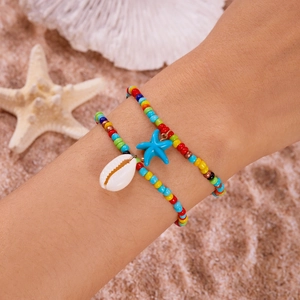 Nahaufnahme von Boho-Perlenarmbändern mit Seestern- und Muschel-Anhängern am Sandstrand