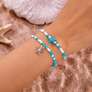 Details von Strandarmbändern mit blauen Perlen und silbernen Seesternen auf Sand