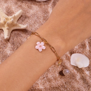 Detailaufnahme des goldenen Büroklammer-Armbands mit rosa Kirschblüten-Anhänger am Strand