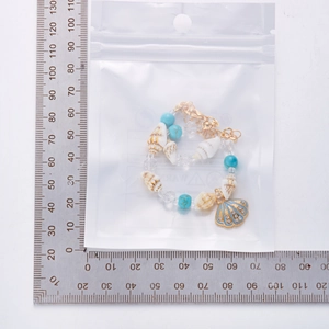 Detail eines Strandarmbands mit Muscheln und türkisfarbenen Perlen auf einem Messlineal