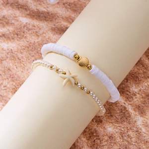 Close-up of layered anklets featuring gold shell charms and white starfish beads