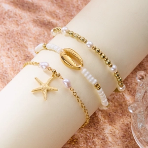 Detail of beach jewelry set featuring starfish, conch charms and white pearls on sand