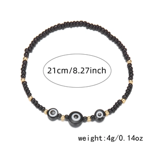 Detail of beaded evil eye anklet featuring black beads and golden accents on a white base