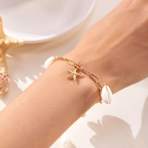 Nahaufnahme des goldenen Seesterns und der weißen Muschel-Anhänger am Gliederkettenarmband