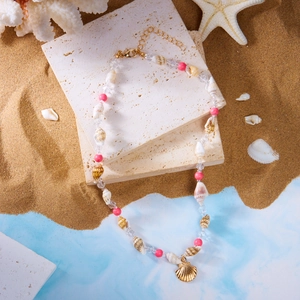 Detail einer Perlenkette mit Muscheln, rosa Perlen und Goldanhänger auf weißem Stein