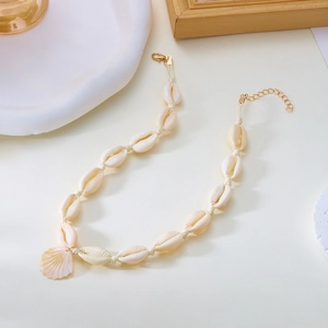 Dettaglio di collana bohémien con conchiglie, ciondolo smerlato dorato e catena intrecciata