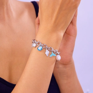 Detail of silver chain bracelet with whale tail, pearl, and shell charms on wrist
