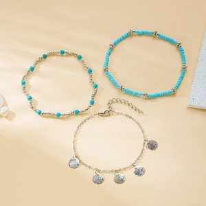 Detail of silver shell charms and blue beaded layered anklets on beach theme background