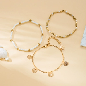 Close-up of gold shell charms and white pearl beads on a layered beach anklet set