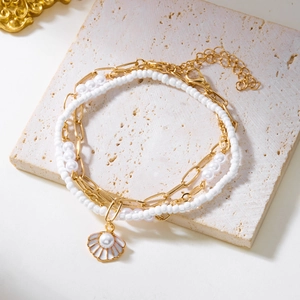 Detail of a layered gold anklet with shell pearl charms on a textured stone surface