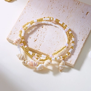 Detail of multi-layer beaded anklet with starfish and seashell charms on stone stand