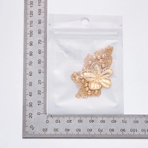 Vue détaillée d'un collier fleur en métal doré dans son emballage avec une règle graduée