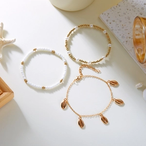 Close-up of bohemian layered anklet with gold shell pendants and white bead details