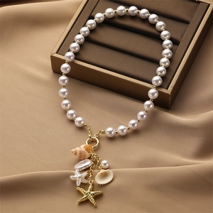 Dettaglio della collana di perle con stella marina dorata e ciondoli a conchiglia su raso
