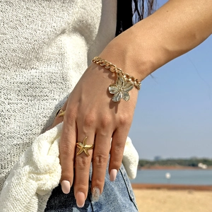 Détail du bracelet fleur dorée et de la bague étoile de mer portés en vacances d'été