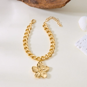 Détail d'un bracelet doré avec pendentif fleur texturé et chaîne à mailles gourmette chic