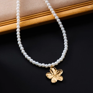 Détail macro d'un collier de perles blanches avec pendentif fleur en or sur plateau bois