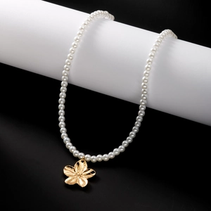 Détail d'un collier de perles blanches avec un pendentif fleur dorée brossée