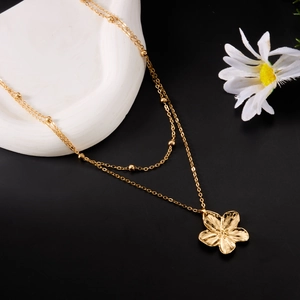 Détail du collier doré multi-rangs avec perles et pendentif fleur sur plateau