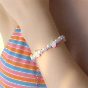 Dettaglio di un bracciale con perle bianche e ciondoli fragola rosa indossato al polso