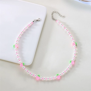 Dettaglio di una dolce collana di perle bianche con ciondoli a fragola rosa