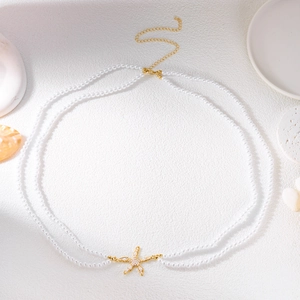 Detail of double-layer pearl body chain with a golden starfish pendant on beach background