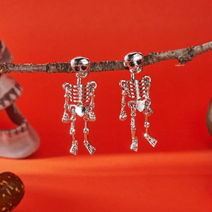 Detailed view of silver skull skeleton earrings hanging on a branch for Halloween decor